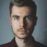 pexels-photo-614810-614810 Close-up portrait of a young man with facial hair and a serious expression.